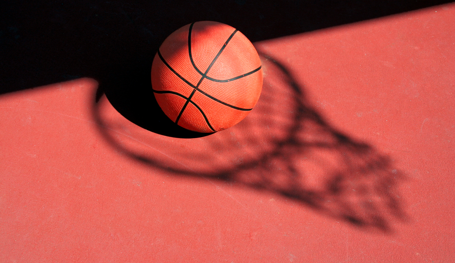 Basketball in a beam of light on a red court